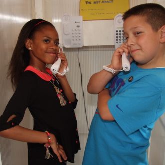 Close-up of two children standing in a telephone booth with phones to their ears, as part of the Children's Republic of Shoreditch project.