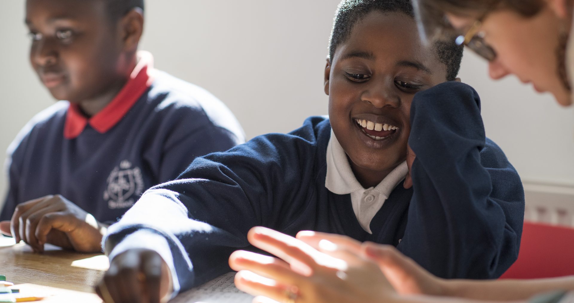 A mentor sitting at a table with two pupils. Writing mentors encourage and support young writers to reach their potential.