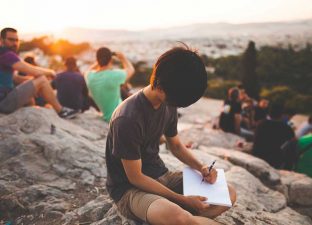 boy sits on a rock writing a letter