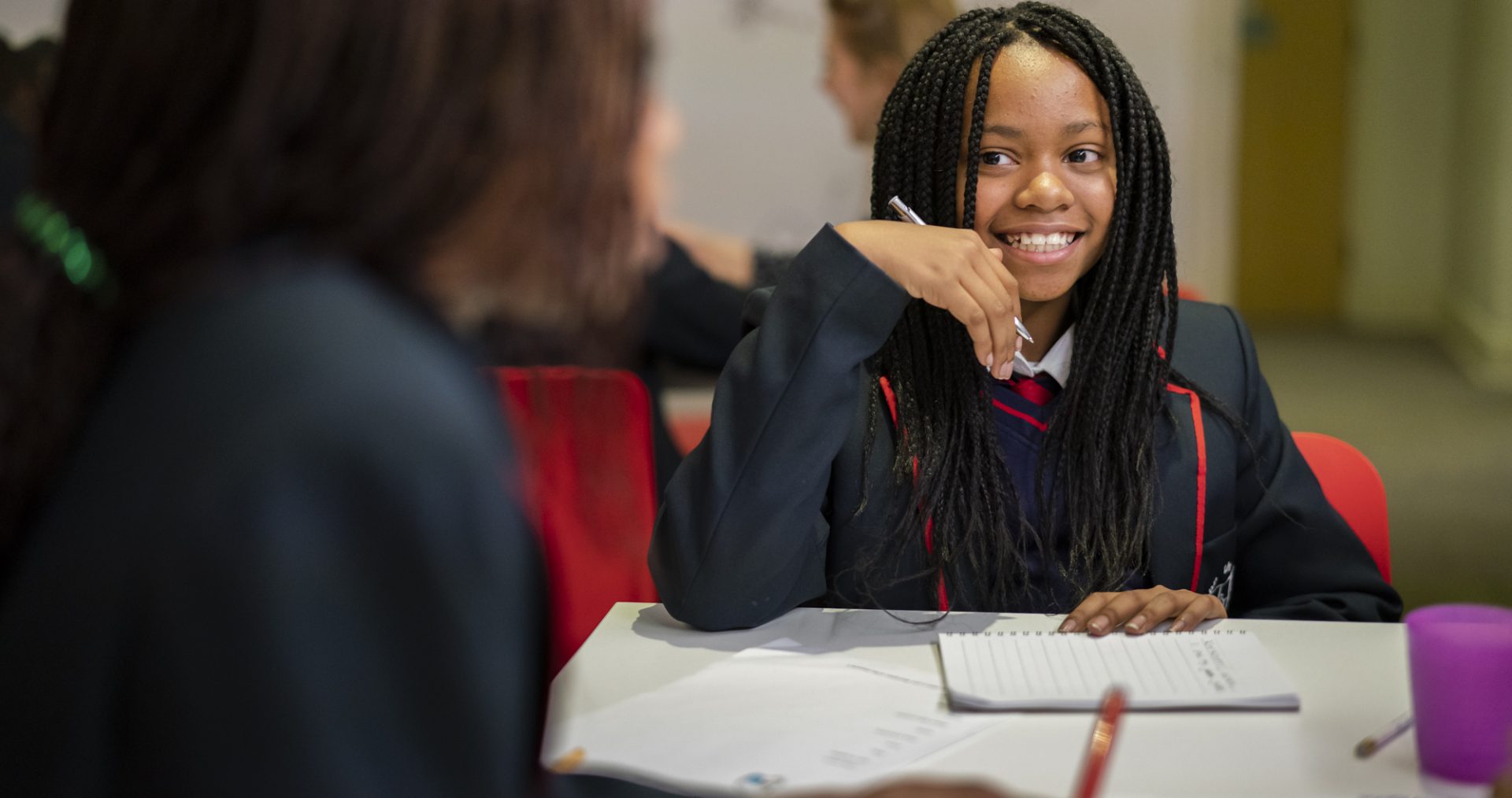 Young writer sitting behind a desk smiling at a volunteer mentor.