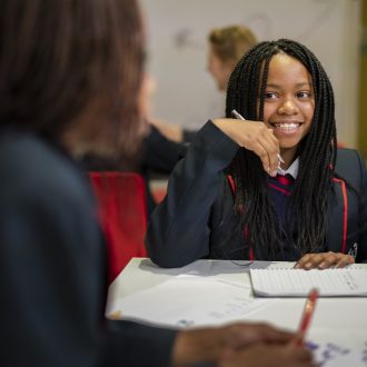 Young writer sitting behind a desk smiling at a volunteer mentor.