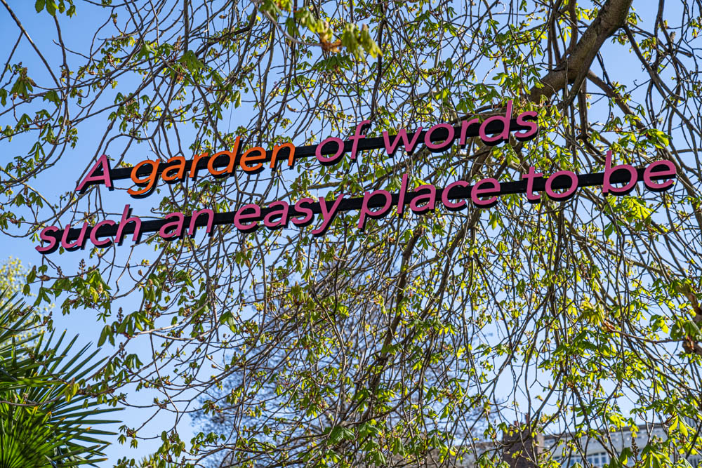 A group of large, pink letters that read 'A garden of words, such an easy place to be' sit high in a tree top