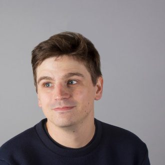 Ed Cornish sits smiling in front of grey background