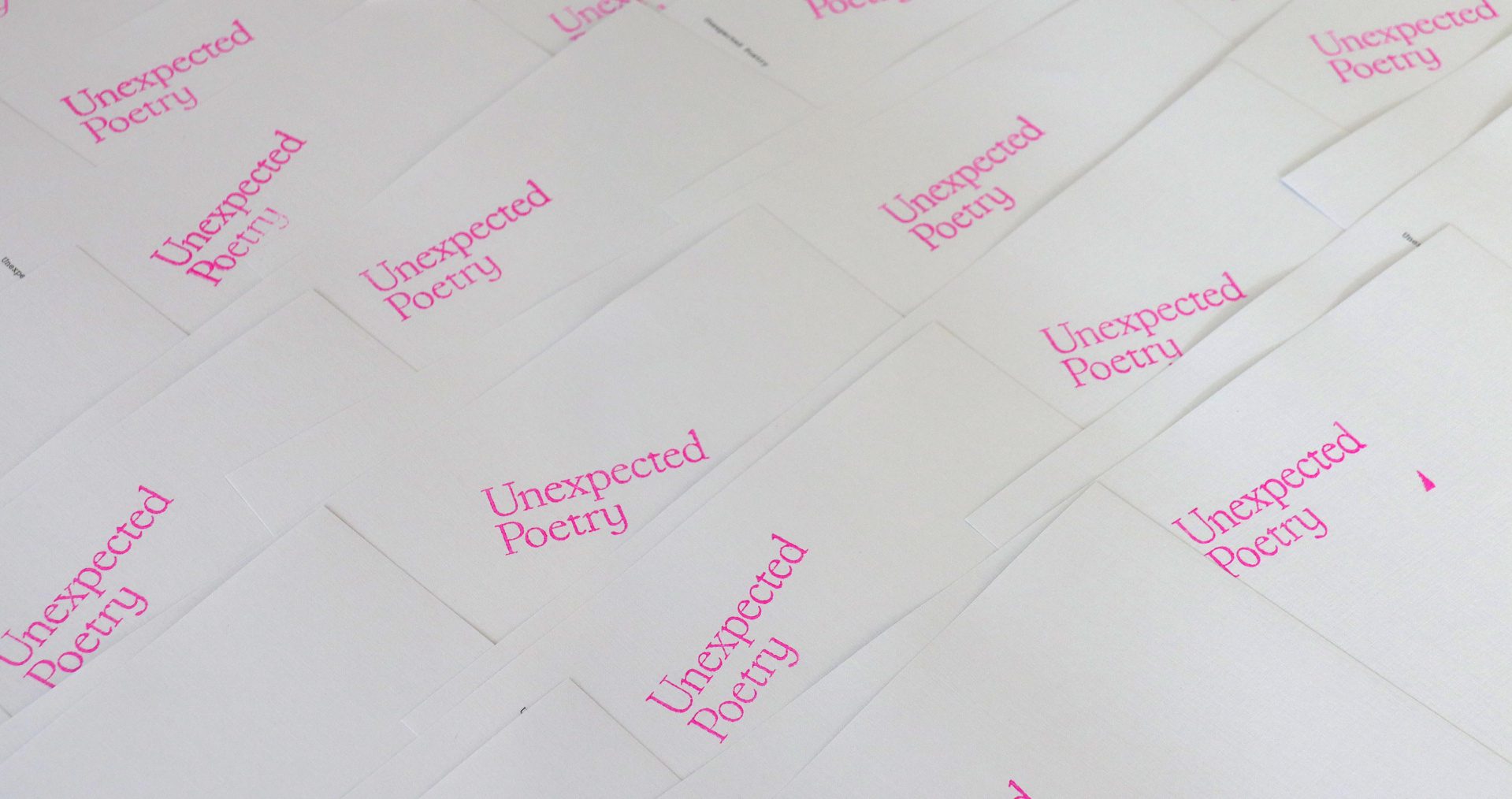 Bright white book covers are laid out in a large pile with 'Unexpected Poetry' stamped in hot pink on top