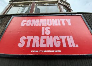 A large billboard with red and pink text proclaims 'community is strength' on Seven Sisters Road, London, UK