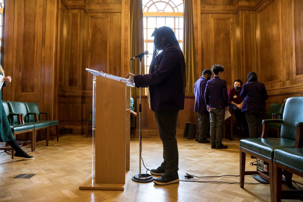 Young person stands silhouetted at a podium ready to give a speech they have written