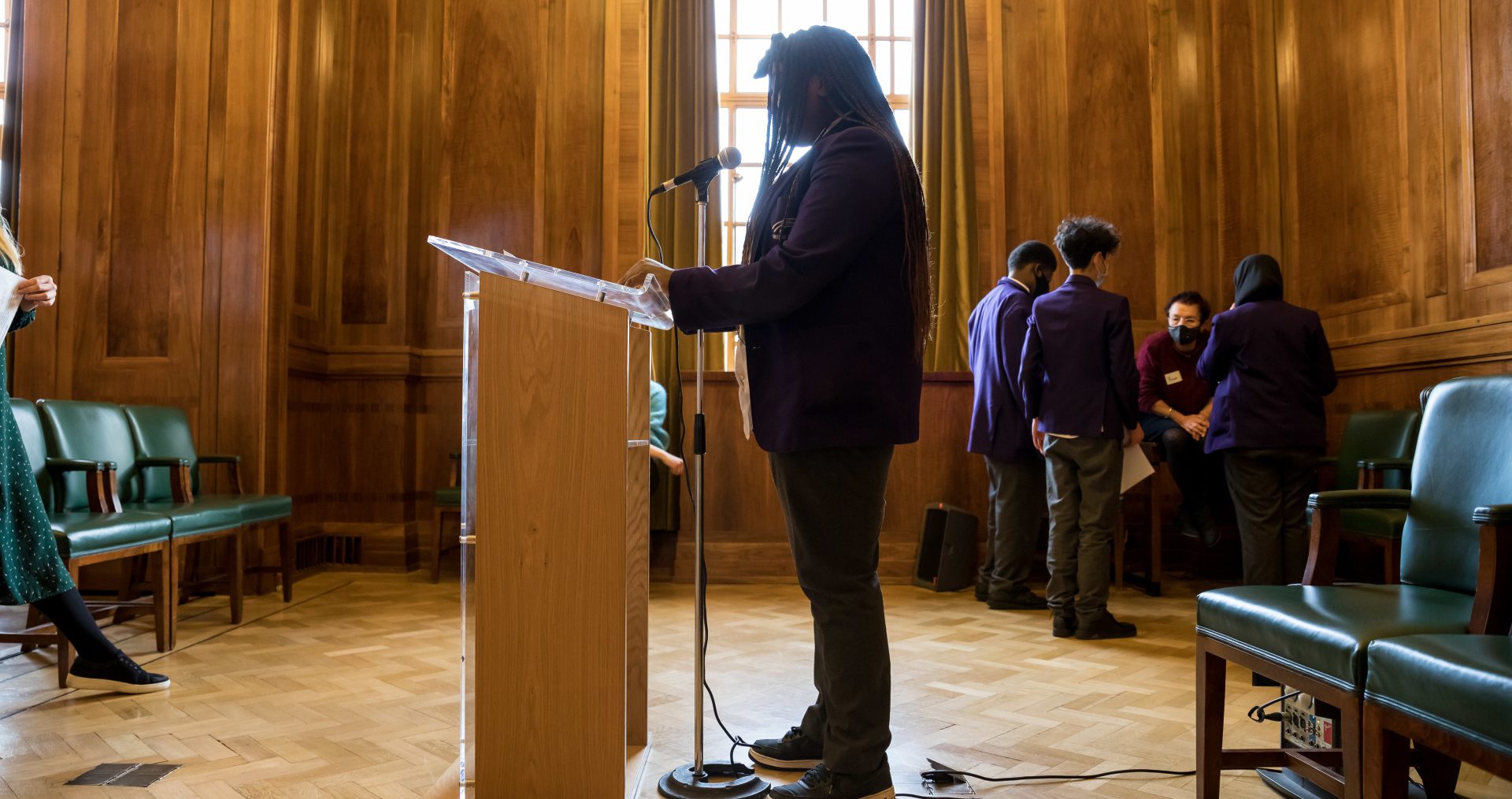 Young person stands silhouetted at a podium ready to give a speech they have written