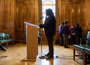 Young person stands silhouetted at a podium ready to give a speech they have written