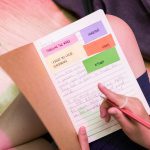 Close up of a child's notebook with a handwritten story in pencil. Coloured paper with writing prompts are stuck on the stop of the page.