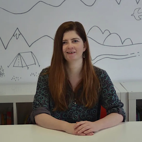 Bronia Evers has long dark hair and sits smiling hands clasped on a white desk.