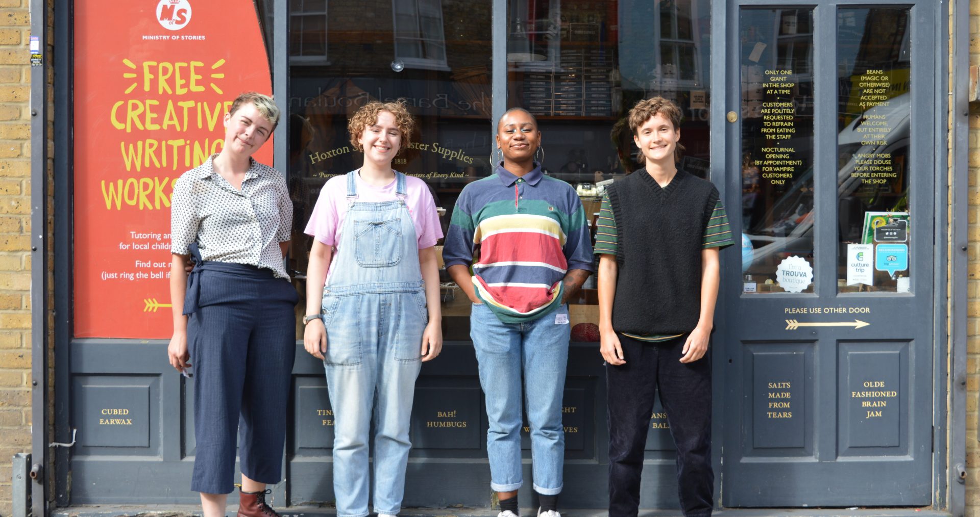 Four happy humans stand in a row, smiling outside Ministry Of Stories shop front.