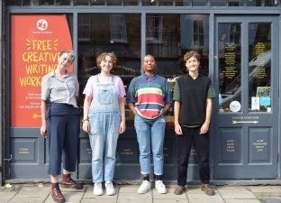 Four happy humans stand in a row, smiling outside Ministry Of Stories shop front.