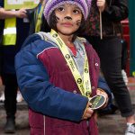 A young writer in winter coat and purple hat looks down at her lime green Monster March medal