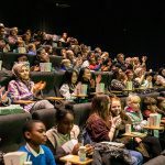 A large cinema audience, seated, watching the screen