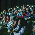 A large cinema audience, seated, watching the screen