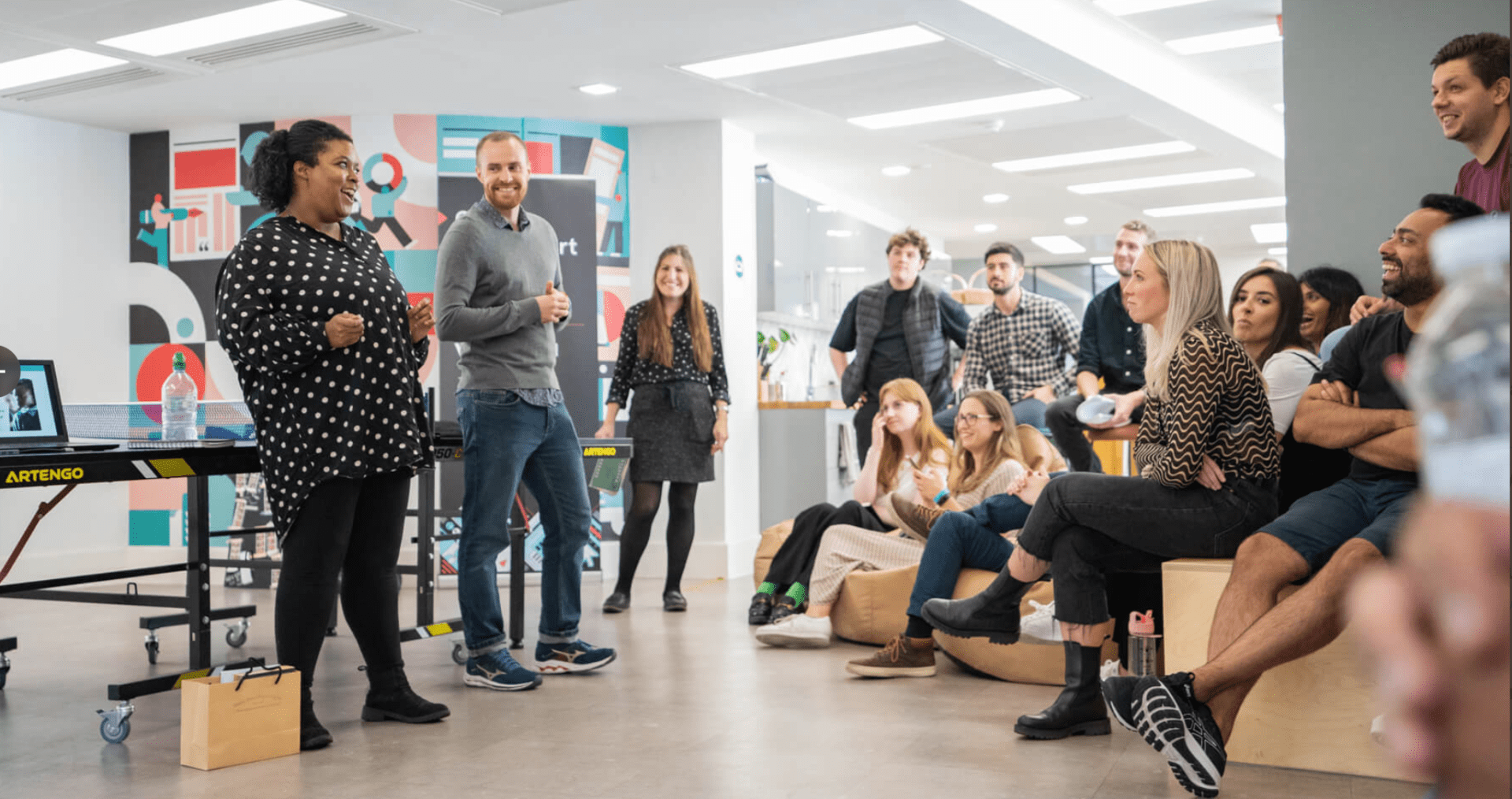 Two team members from Ministry of Stories stand in smiling in front of a group at Raconteur office.