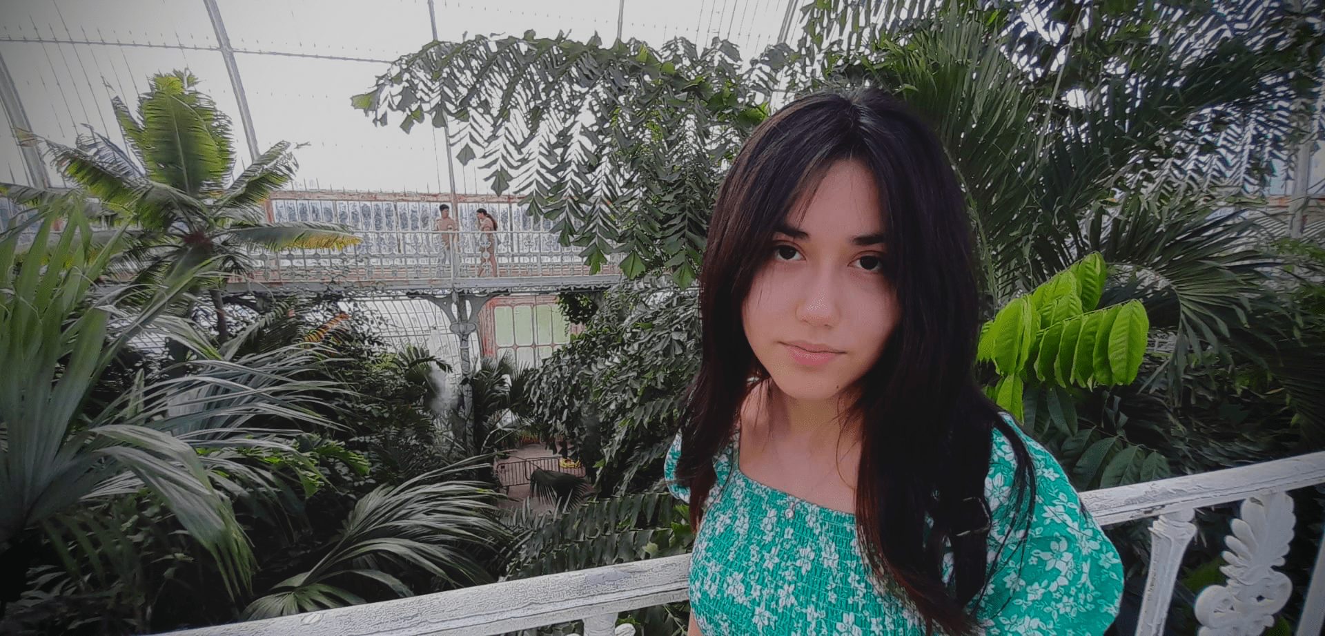 Joanna, with long dark hair, stands looking directly at the camera wearing a light green top.