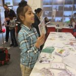 A young writer chats with a visitor smiling and showing them their Zine