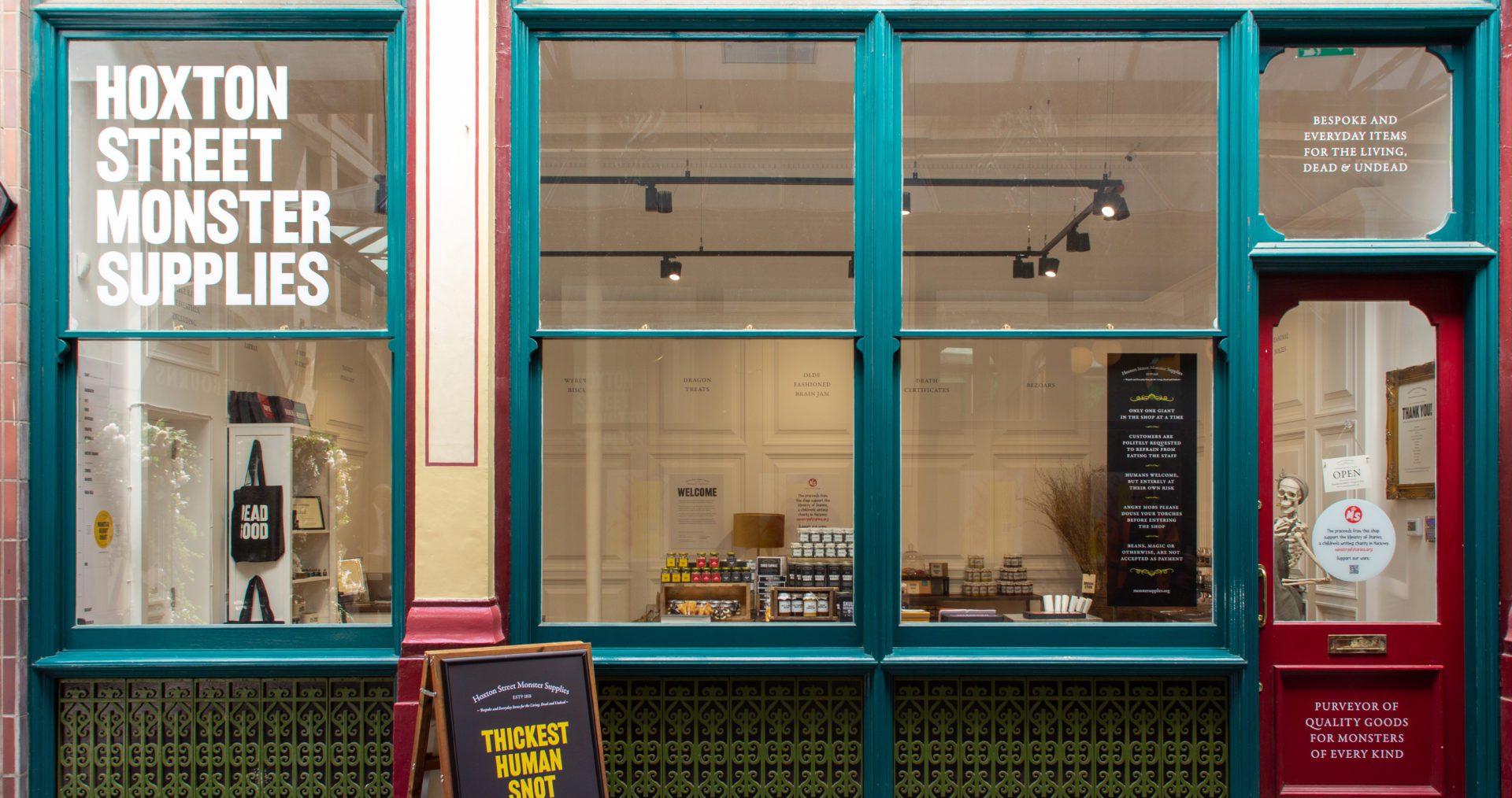 An orante store front with green and red metal frame and a skeleton standing at teh door