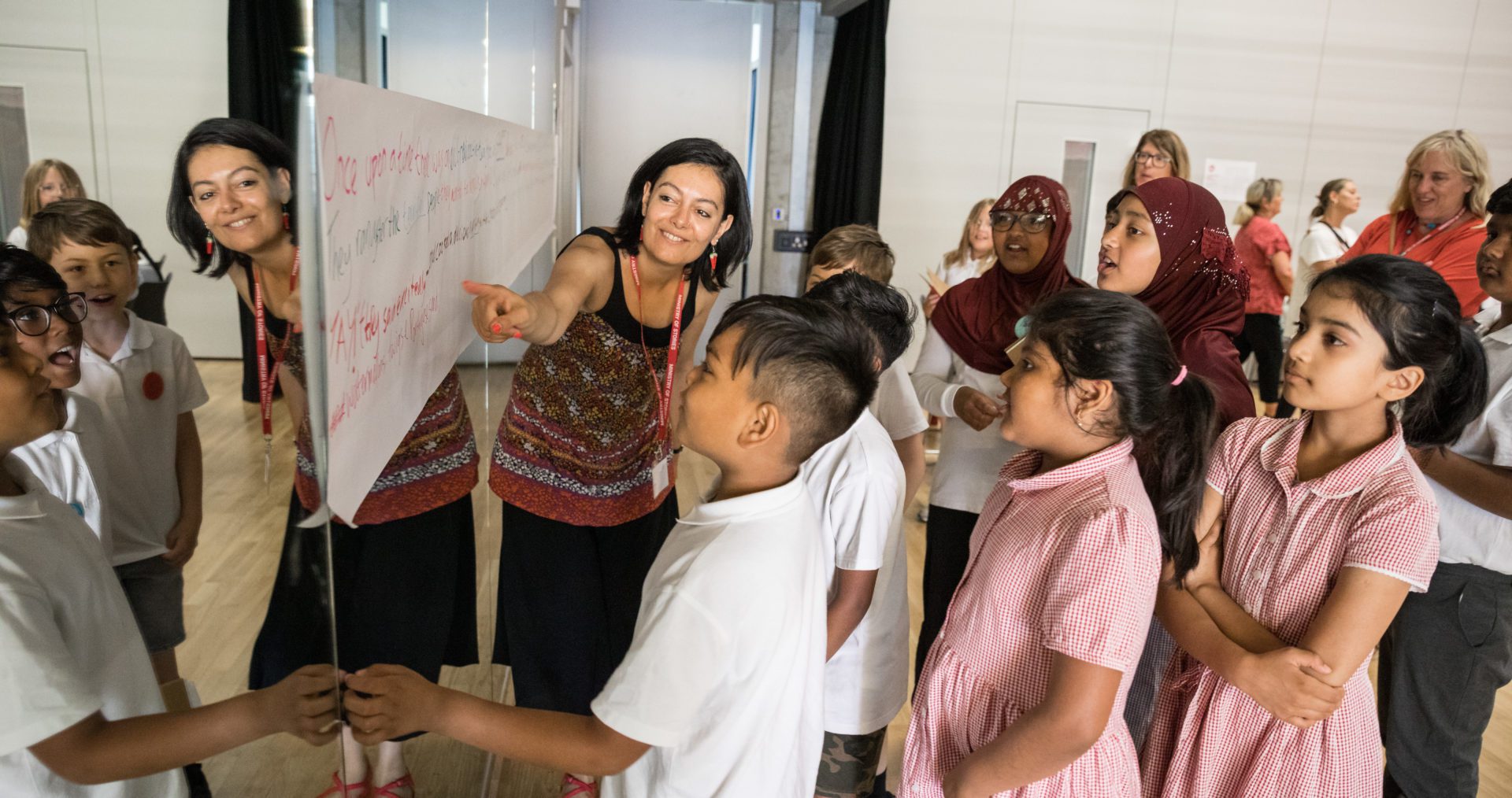 A photo of one of our writing facilitators with a group of young people, showing them a flipchart full of ideas