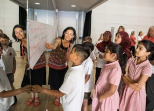 A photo of one of our writing facilitators with a group of young people, showing them a flipchart full of ideas