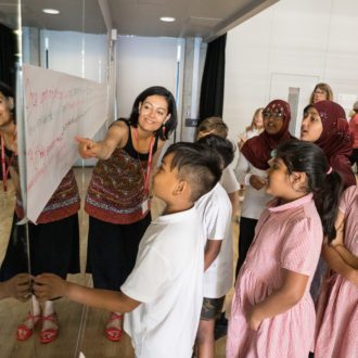 A photo of one of our writing facilitators with a group of young people, showing them a flipchart full of ideas