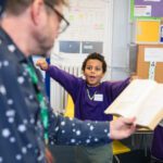 A young boy with a purple jumper and short hair jumps excitedly at some poetry read by a writing facilitator