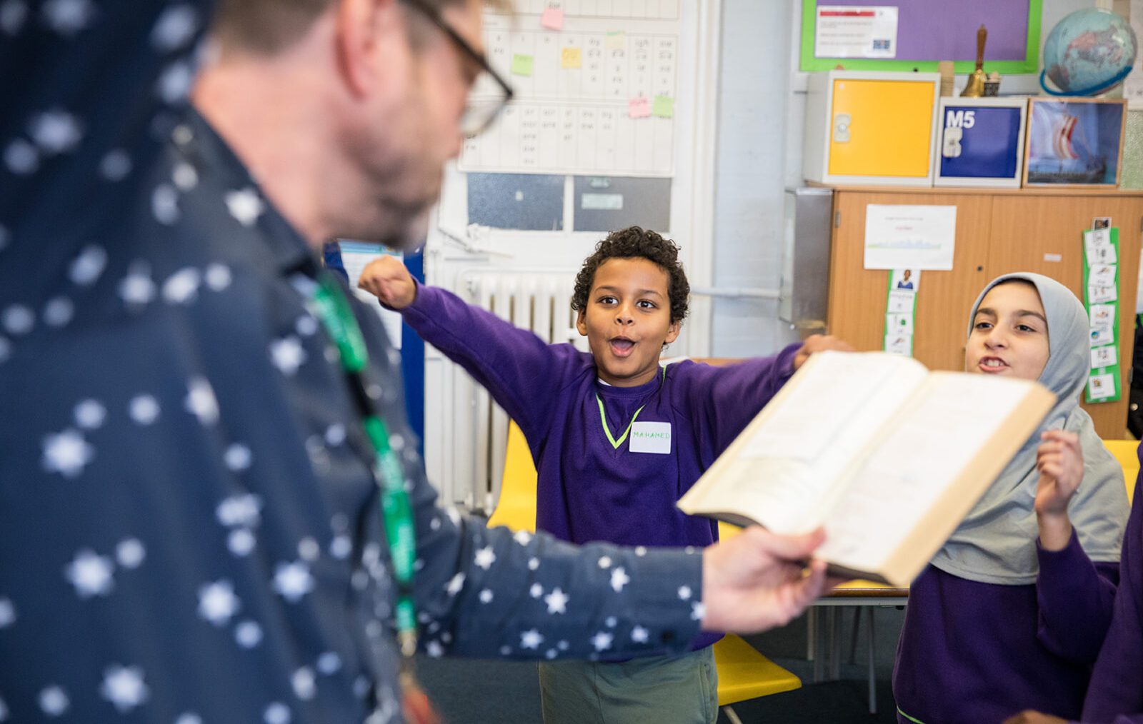 A young boy with a purple jumper and short hair jumps excitedly at some poetry read by a writing facilitator