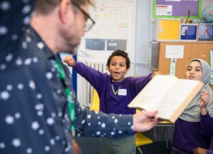 A young boy with a purple jumper and short hair jumps excitedly at some poetry read by a writing facilitator