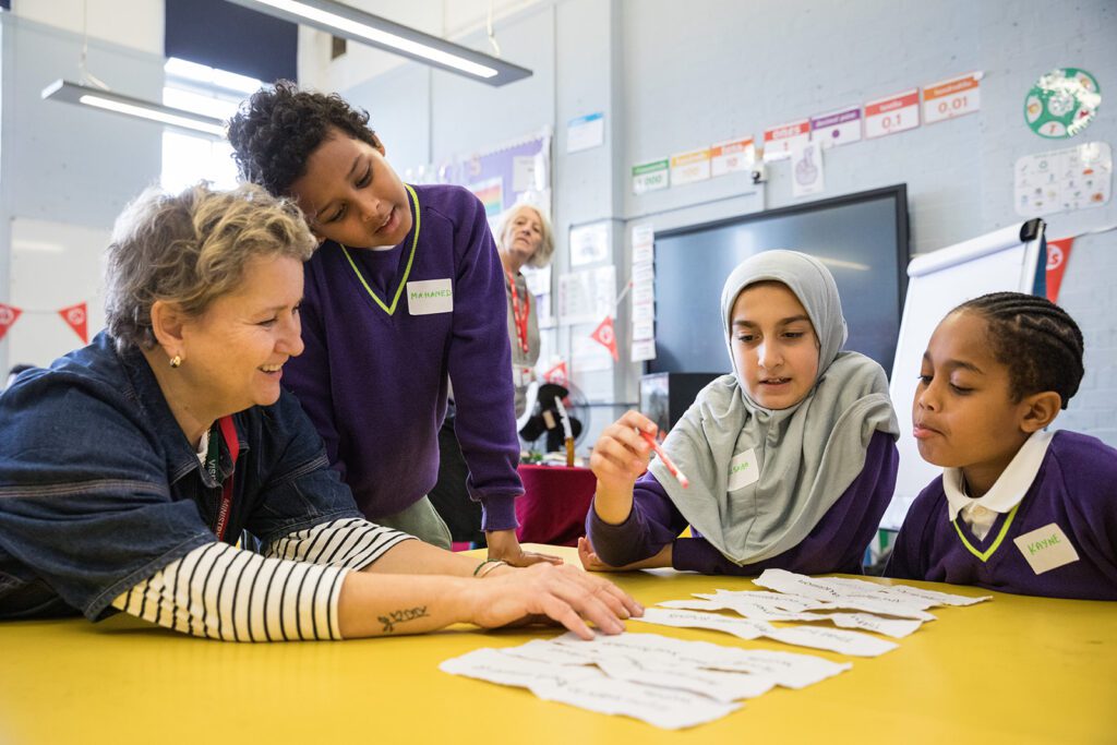 Three young people sit at a table with a writing facilitator smiling and laughing laying out words on strips of paper
