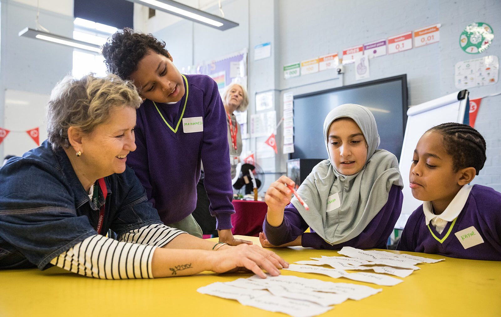 Three young people sit at a table with a writing facilitator smiling and laughing laying out words on strips of paper