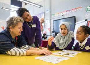 Three young people sit at a table with a writing facilitator smiling and laughing laying out words on strips of paper