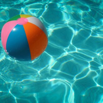 A colourful striped beach ball floats on top of bright blue swimming pool water.