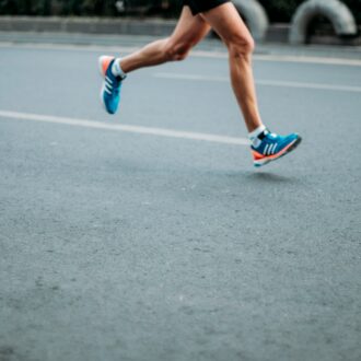 a runner runs down a grey concrete road, we see there legs and feet in blue and orange trainers.