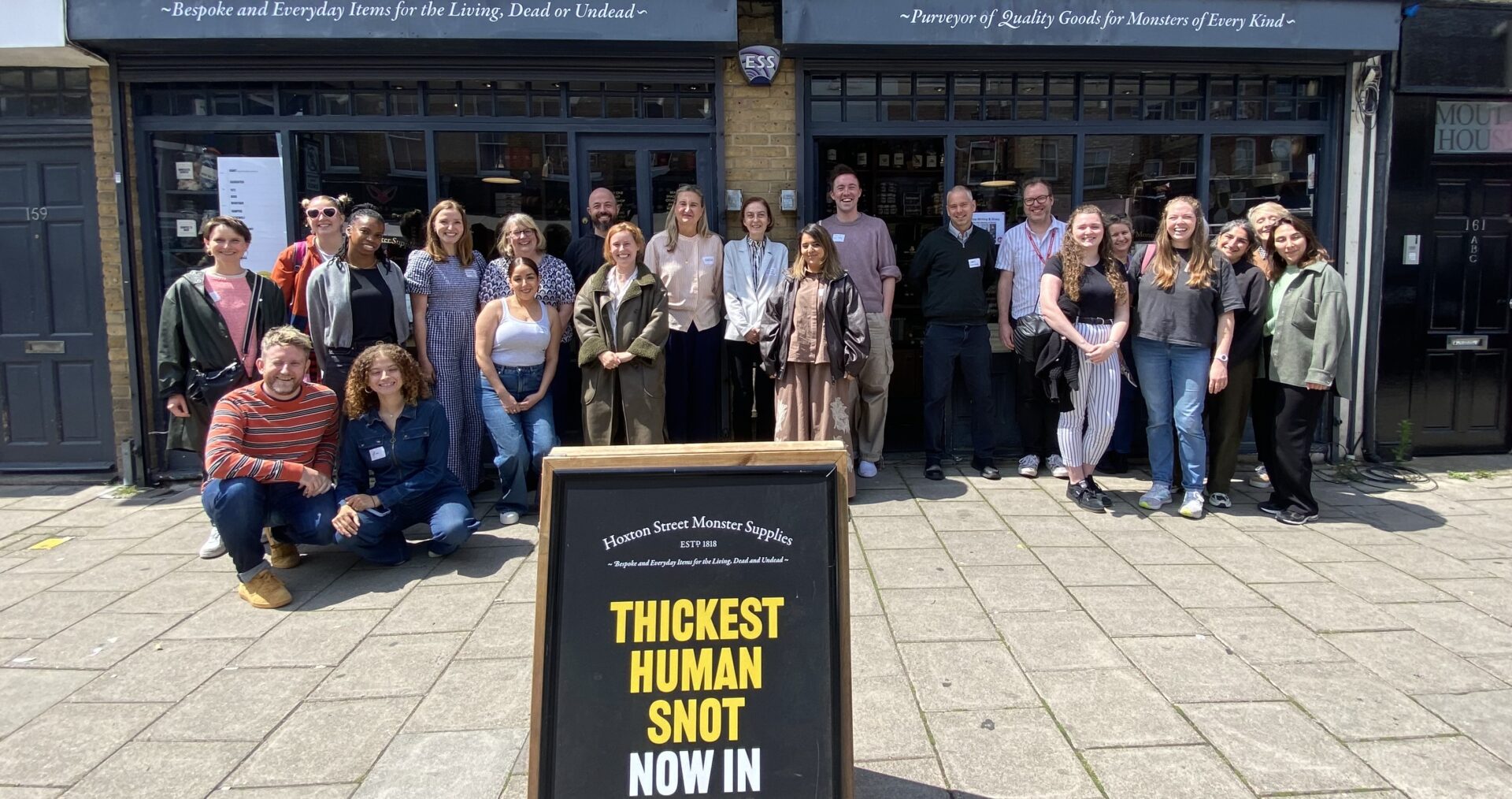 A large group of teachers stand cheering in front of the store front Hoxton Street Monster Supplies.