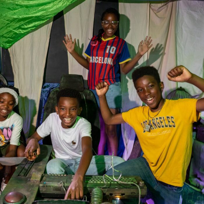 Four young black teenagers celebrate with big smiles and arms in the air, as they work out a puzzle in the Ministry of Stories escape room 