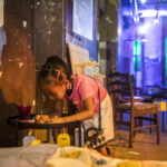 A young girl leans over to write her dream on a luggage tag, ready to hang it up among the bright lights and clouds