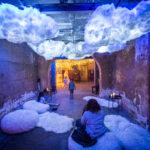 A small room glows blue and white with fluffy luminous clouds hanging from the celling and inventing fluffy rugs laying across the floor.