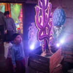 A young boy looks up in awe at a dramatically lit magical flower, made out of cardboard. He is in the Botanist's room in DreamState, an exhibition of young people's writing and ideas.