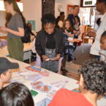 A group of young people and adults look around a zine fair, where young writers are presenting the zines they have made.
