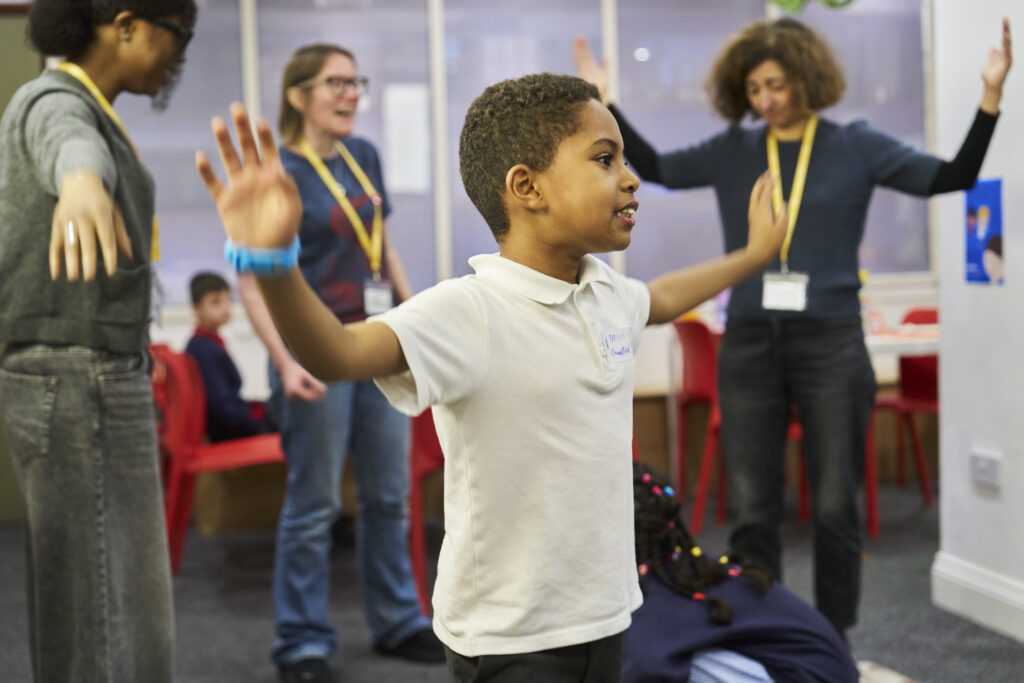 A young writer stands in Ministry HQ with his arms out, playing a game.
