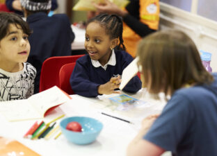Two young writers and a writing mentor sit around a table at our writing centre, discussing ideas. They are smiling and chatting.