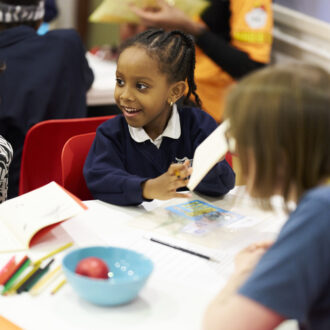 Two young writers and a writing mentor sit around a table at our writing centre, discussing ideas. They are smiling and chatting.