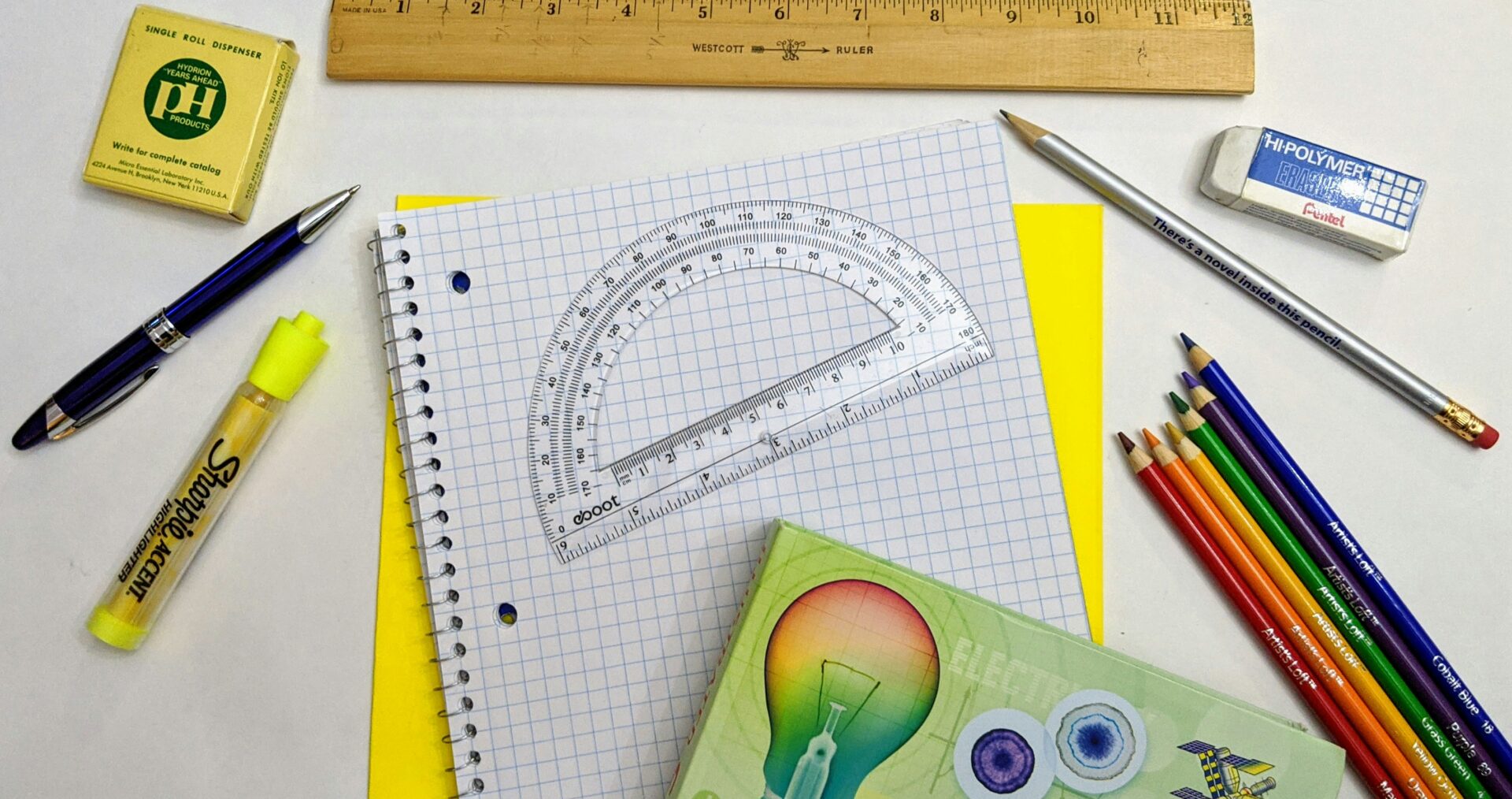School supplies including pencils, ruler and notebook are spread out over a white table