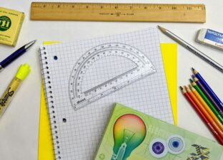 School supplies including pencils, ruler and notebook are spread out over a white table