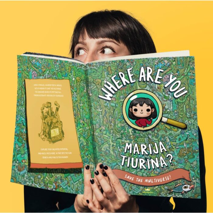 A woman's head - with dark hair in a bob style - pops up from behind a large children's book titled Where are we? 