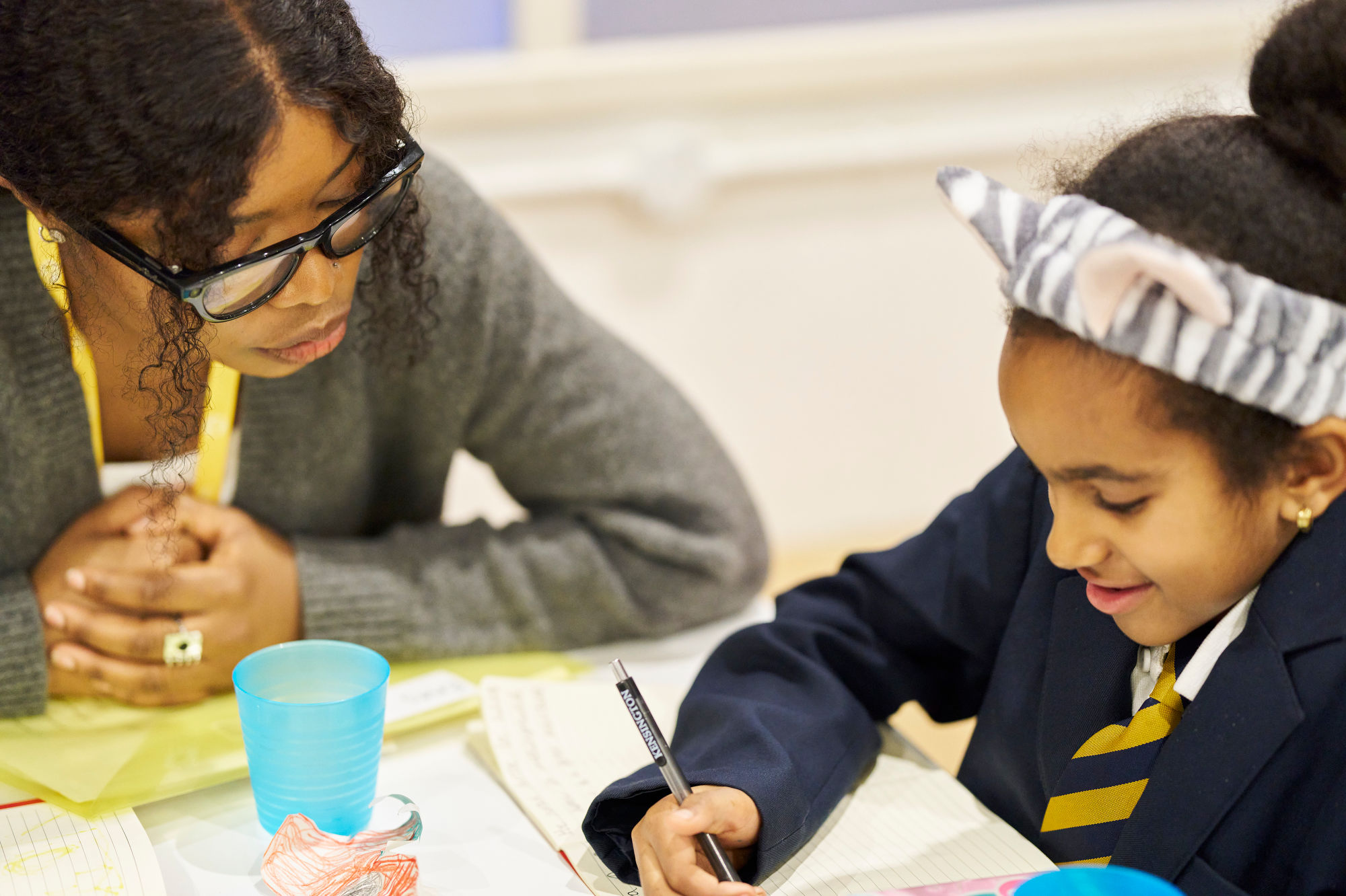 volunteer writing mentor and child sit at table and complete writing activity together