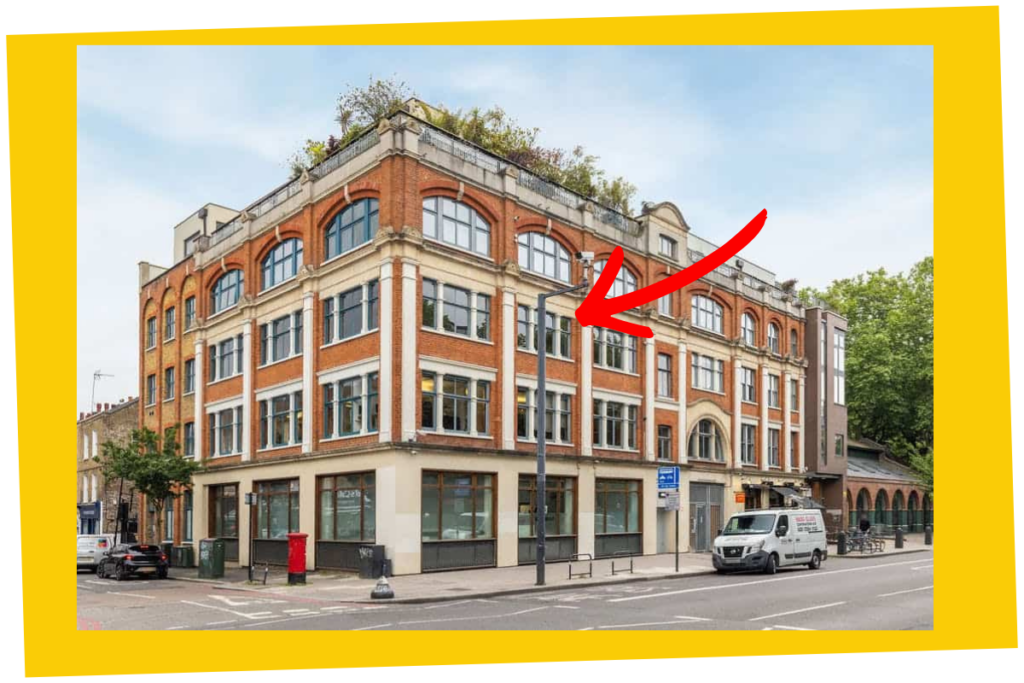 A grand, red brick, four story building sits next o the road. It has large, victorian windows and arches. There is a red arrow pointing to the second floor, showing where the new space for Ministry of Stories is.