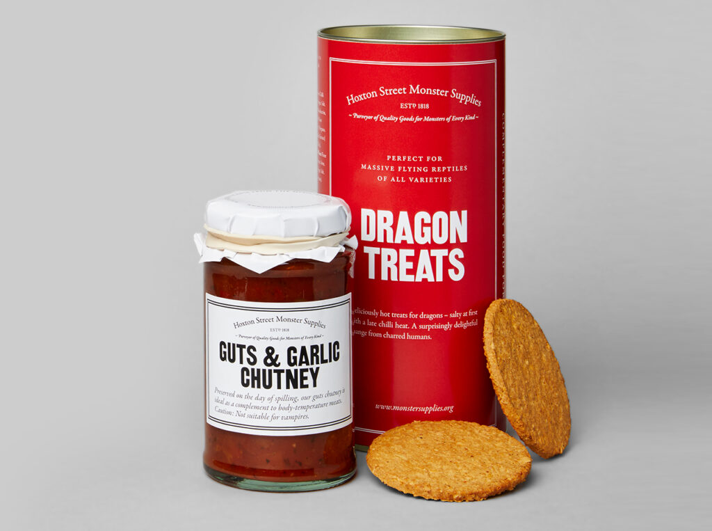 A red tin of biscuits reading Dragon treats sits next to a glass jar - similar to a classic jam jar - that treads Guts and Garlic chutney.