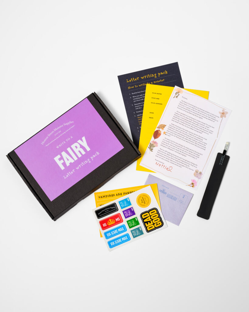 A black letter box with a big purple sticker that reads Fairy, open to show a letter from a fairy, fun colourful stickers, writing sheets, pencil and envelope